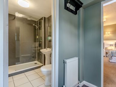 A bathroom with a shower, toilet, and sink next to a hallway leading to a bedroom at The Boars Head Pub in Bishop's Castle