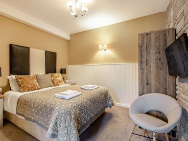 A bedroom with a double bed two bedside tables lamps a chair a wall-mounted television and a wardrobe at The Boars Head Pub Bishop's Castle