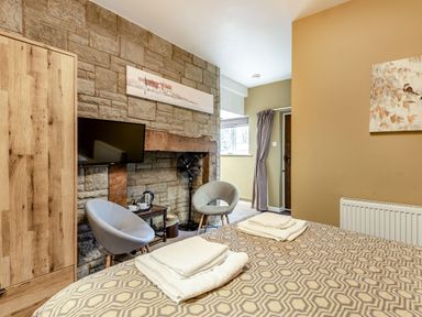 A bedroom with a patterned bedspread two chairs a wooden wardrobe a TV mounted on a stone wall and a small table with a kettle at The Boars Head Pub in Bishop's Castle