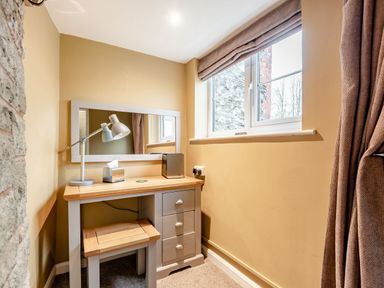 A small desk with a stool a lamp tissue box and mirror next to a window in a room at The Boars Head Pub in Bishop's Castle