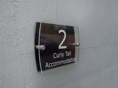 A wall-mounted black sign with the number 2 and the text Curly Tail Accommodation