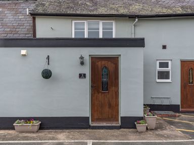 Exterior of a grey building with wooden doors and flower pots at The Boars Head Pub in Bishops Castle