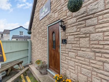 An entrance door to Curly Tail accommodation with stone walls wooden door flowers and a wooden bench outside