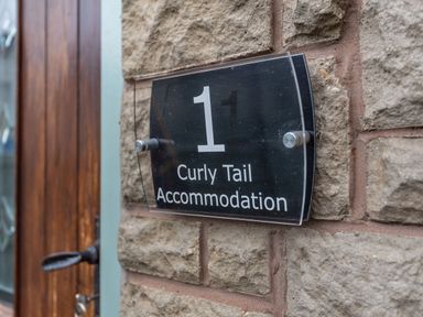 A house number plaque reading 1 Curly Tail Accommodation mounted on a stone wall next to a wooden door