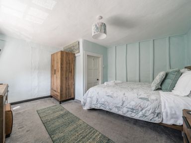 A bedroom with a bed with pillows and blanket a wooden wardrobe a rug and a door at The Boars Head Pub in Bishop's Castle
