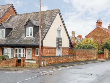 A brick and stucco house with a tiled roof on a street corner with a brick wall and greenery at Little Wash Cottage in Hunstanton