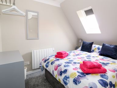 A bedroom with a bed with colorful bedding two dark cushions and pink towels under a skylight window at Little Wash Cottage in Hunstanton