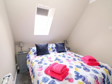 A bedroom with a bed under a skylight window with colorful bedding and towels on the bed at Little Wash Cottage in Hunstanton