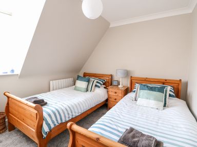 A bedroom with two single wooden beds with striped bedding and pillows and a wooden nightstand with a lamp between them at Little Wash Cottage in Hunstanton