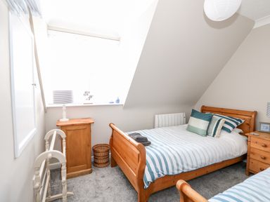 A bedroom with two wooden beds with striped bedding a wooden cabinet a bedside table and a window at Little Wash Cottage in Hunstanton