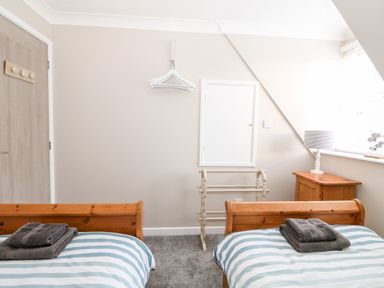A bedroom with two single wooden beds with striped bedding and folded towels on top at Little Wash Cottage in Hunstanton