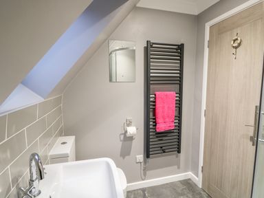 A bathroom with a sink toilet small mirror towel radiator with pink towel and wooden door at Little Wash Cottage in Hunstanton