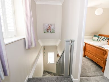 A stairway with gray carpet and railing next to a bedroom with a wooden bed at Little Wash Cottage in Hunstanton