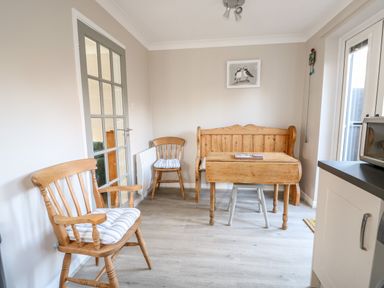 A dining area with wooden chairs a bench and a table next to glass doors at Little Wash Cottage in Hunstanton