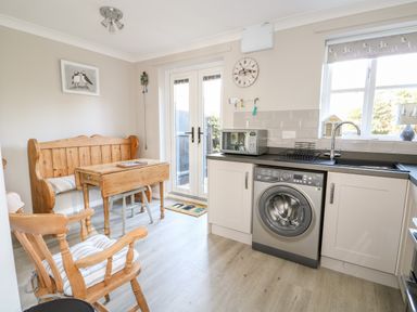 A kitchen area with wooden bench seating a wooden table and chairs beside a washing machine microwave and sink at Little Wash Cottage in Hunstanton