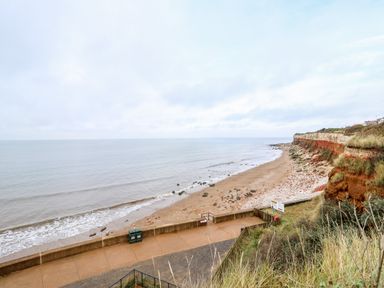 A coastal path along a sandy and rocky beach with cliffs and grass at Little Wash Cottage in Hunstanton