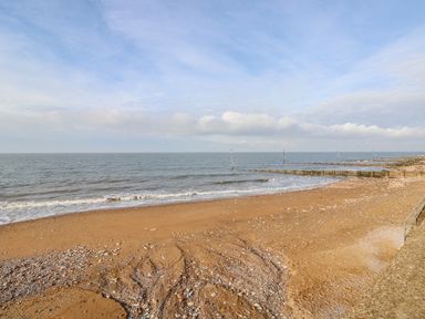 A sandy beach with scattered shells and wooden groynes extending into the sea at Little Wash Cottage in Hunstanton
