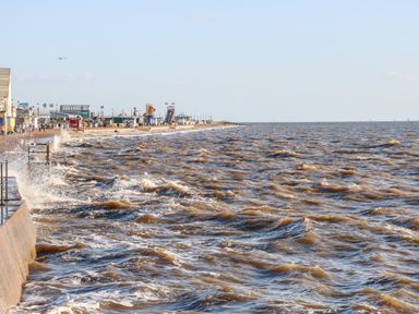 A waterfront with waves crashing on a concrete barrier and buildings along the shore at Little Wash Cottage in Hunstanton