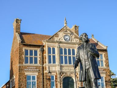 A statue of a man with a cane in front of a stone town hall building with a clock and tourist information signs at Little Wash Cottage in Hunstanton