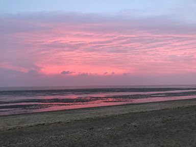 A beach with wet sand and water under a pink and purple cloudy sky at Little Wash Cottage in Hunstanton