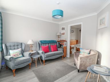A living room with two grey armchairs a grey sofa with red cushions a beige armchair and two small round tables at Little Wash Cottage in Hunstanton