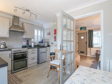 A kitchen with stove, kettle, toaster, wooden chair, and glass door leading to a living room at Little Wash Cottage in Hunstanton