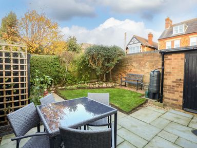 A garden with a patio table and chairs a wooden bench and grass at Little Wash Cottage in Hunstanton