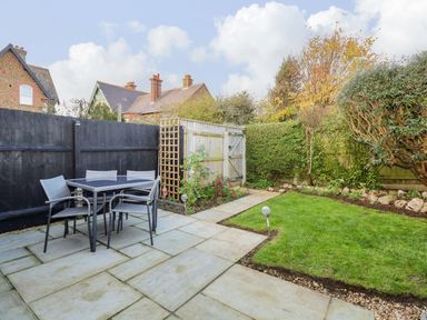 A garden with patio furniture a lawn hedge and a wooden gate at Little Wash Cottage in Hunstanton