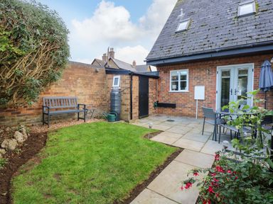 A small garden with grass lawn stone pathway bench table and chairs outside a brick house at Little Wash Cottage in Hunstanton