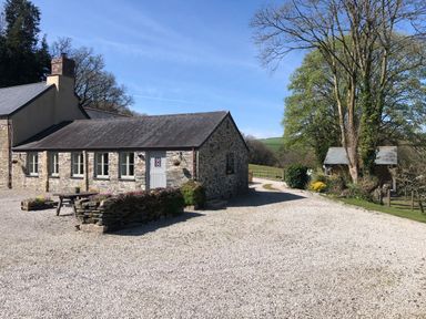 Stone cottage with a gravel driveway and trees surrounding a garden at Mimis Cottage in St Neot