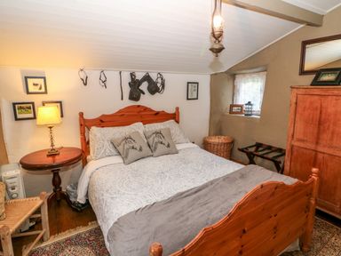 A bedroom with a wooden bed and horse-themed pillows a wooden side table with a lamp a wicker basket and a wooden wardrobe at Mary Rose Cottage in Cordal near Castleisland County Kerry