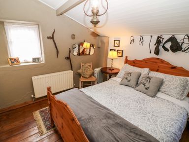 A bedroom with a wooden bed with patterned bedding and horse pillows a wooden chair and a side table with a lamp at Mary Rose Cottage in Cordal near Castleisland County Kerry