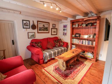 A living room with red sofas a wooden coffee table a bookshelf and framed pictures on the walls at Mary Rose Cottage in Cordal near Castleisland County Kerry