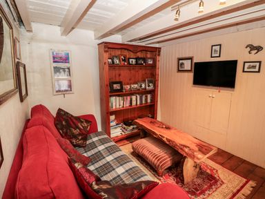 A small living room with a red sofa pillows wooden bookshelf books a wooden coffee table an ottoman wall mounted tv framed pictures and a patterned rug at Mary Rose Cottage in Cordal near Castleisland County Kerry