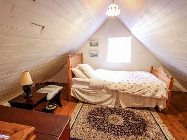 A bedroom with a wooden bed, a side table with a lamp, a bench, and a rug on a wooden floor at Mary Rose Cottage in Cordal near Castleisland County Kerry