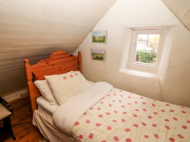 A small bedroom with a wooden bed and floral bedding under a slanted ceiling at Mary Rose Cottage Cordal near Castleisland County Kerry