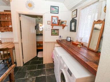 A laundry room with a washing machine and dryer under a wooden countertop next to a door opening to a bathroom at Mary Rose Cottage in Cordal near Castleisland County Kerry