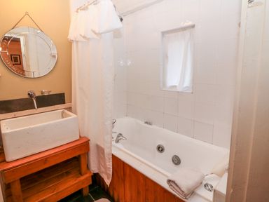 A bathroom with a bathtub a round mirror a sink with wooden stand and a shower curtain at Mary Rose Cottage in Cordal near Castleisland County Kerry