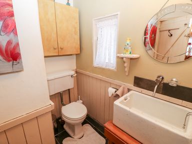 A small bathroom with a toilet wood cabinet a rectangular sink mirror and lace curtain at Mary Rose Cottage Cordal near Castleisland County Kerry