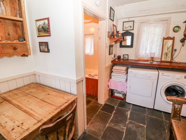 A laundry room with washing machine dryer wooden table and chair stacked towels and a window at Mary Rose Cottage in Cordal near Castleisland County Kerry