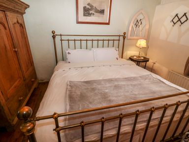 A bedroom with a metal bed frame white bedding a wooden wardrobe a bedside table with a lamp and a framed picture on the wall at Mary Rose Cottage in Cordal near Castleisland County Kerry