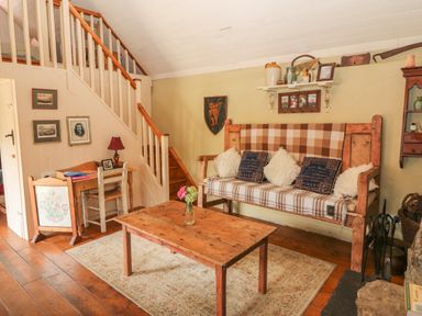 A sitting area with a wooden bench covered with cushions and a plaid blanket alongside a wooden coffee table and a small desk under stairs at Mary Rose Cottage in Cordal near Castleisland County Kerry