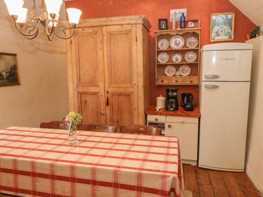 A dining room with a red and white checkered tablecloth on a table and a wooden cabinet and fridge against the wall at Mary Rose Cottage in Cordal near Castleisland County Kerry