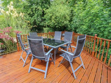 An outdoor wooden deck with six metal mesh chairs around a glass table surrounded by green trees and plants at Mary Rose Cottage in Cordal near Castleisland County Kerry