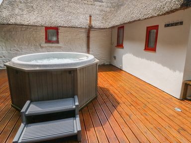 An outdoor hot tub with steps on a wooden deck next to a white building with red window frames at Mary Rose Cottage Cordal near Castleisland County Kerry