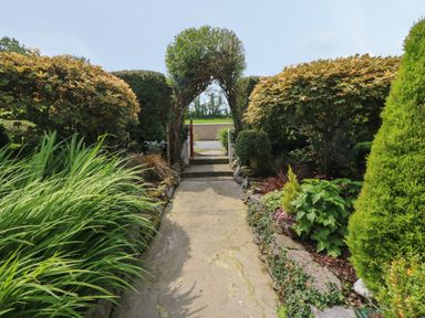 A garden pathway with a green archway surrounded by bushes and plants at Mary Rose Cottage Cordal near Castleisland County Kerry
