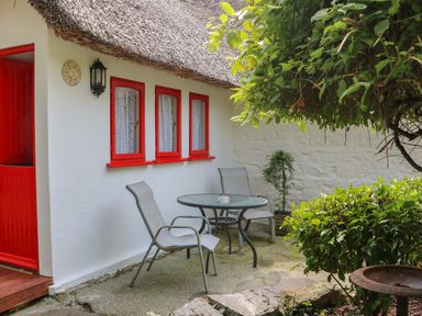 An outdoor patio with two metal chairs and a glass table outside a white cottage with red window frames and a red door at Mary Rose Cottage in Cordal near Castleisland County Kerry
