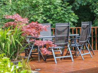 An outdoor wooden deck with a glass table surrounded by six black mesh chairs and plants at Mary Rose Cottage in Cordal near Castleisland County Kerry