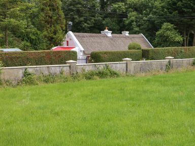 A thatched cottage behind trimmed hedges and a stone wall with a green lawn in front at Mary Rose Cottage in Cordal near Castleisland County Kerry
