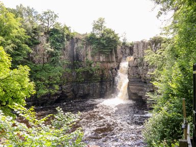 A waterfall flowing into a river surrounded by rocky cliffs and trees at Badgers Sett in Winston near Staindrop